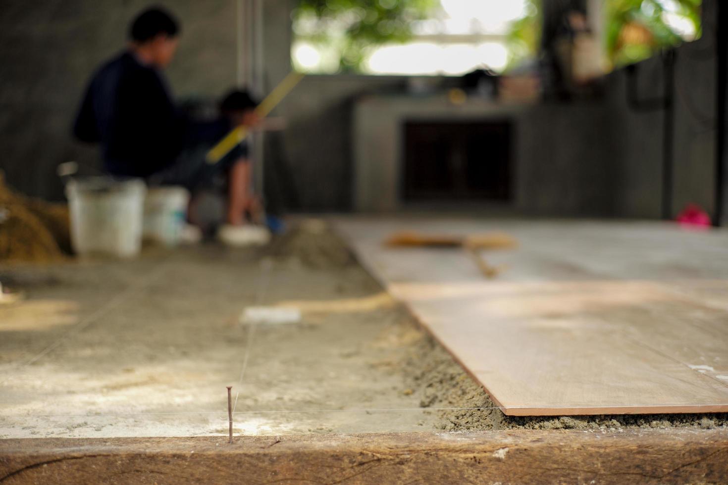 closeup-floor-tiles-on-the-mixed-cement-with-nylon-for-leveling-in-the-house-under-construction-with-blurred-workers-in-the-background-free-photo